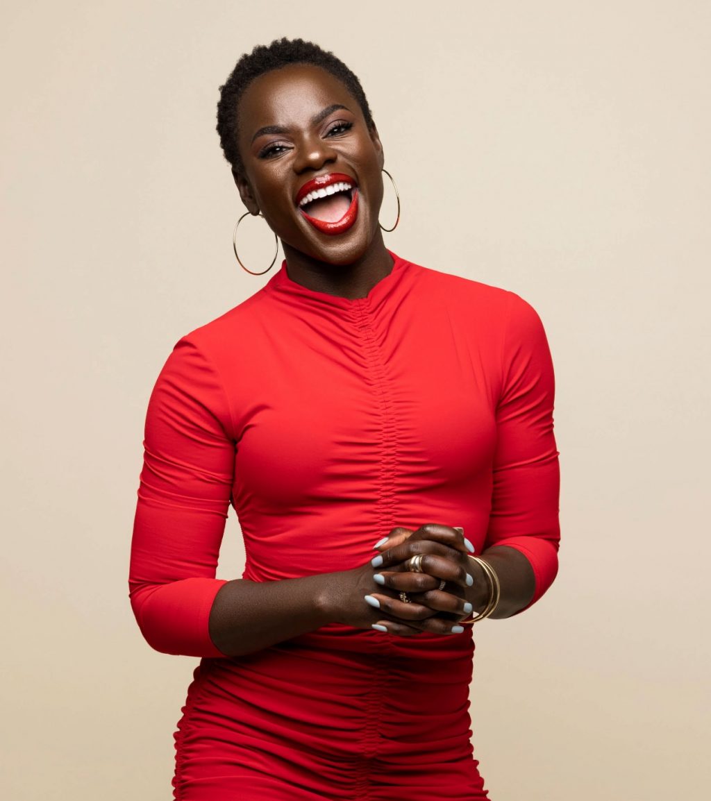 Peloton instructor and author Tunde Oyeneyin smiling in a red top